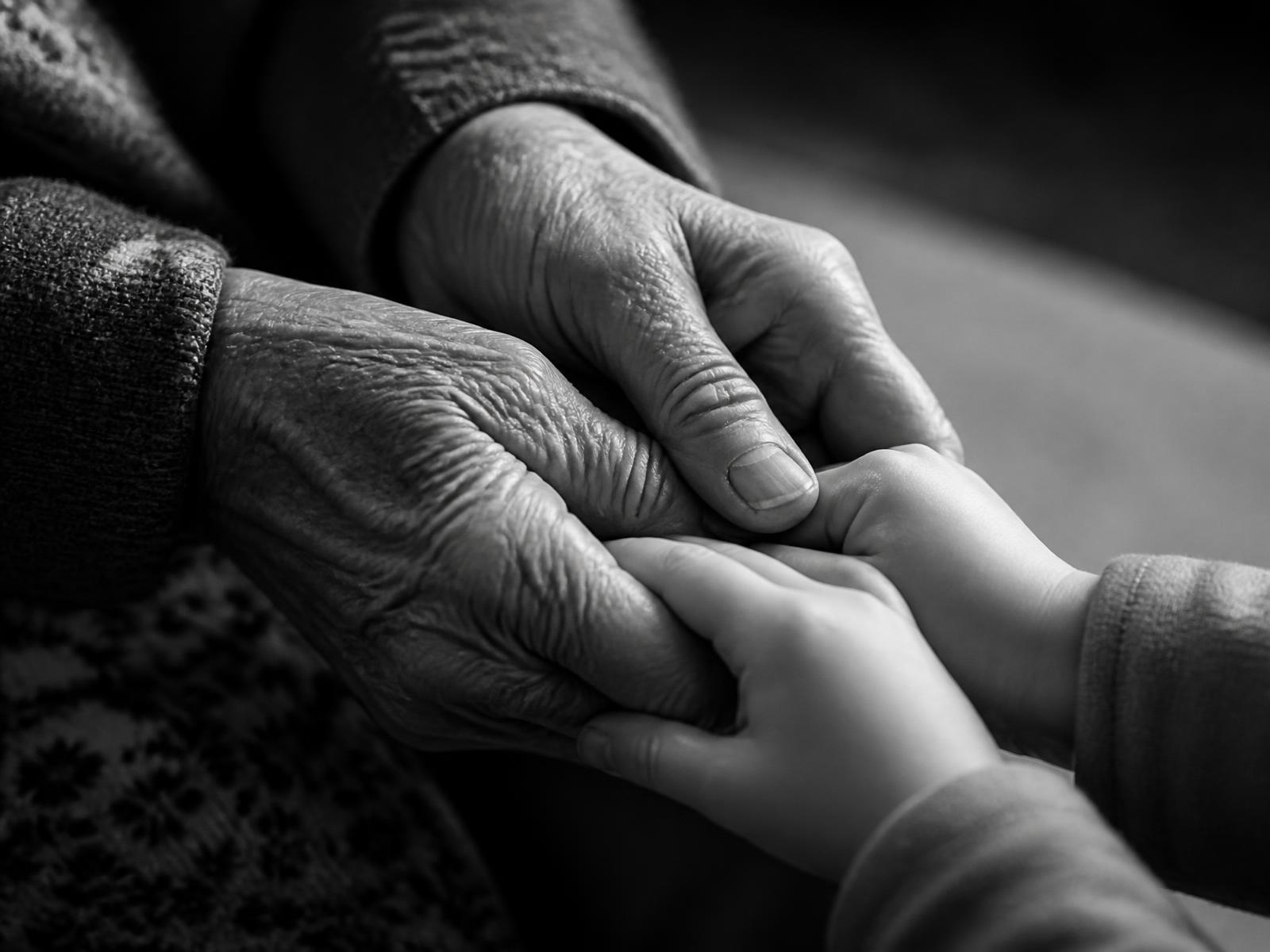 An elderly woman's hands holding a small child's hands